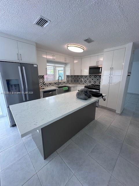 641 SW 99th Pl, Miami, FL 33174 - kitchen with stainless steel appliances, decorative backsplash, white cabinets, a kitchen island, and a textured ceiling