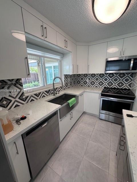 641 SW 99th Pl, Miami, FL 33174 - kitchen featuring appliances with stainless steel finishes, decorative backsplash, white cabinetry, a textured ceiling, and light stone counters