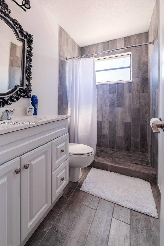 203 SE 8th St, Dania Beach, FL 33004 - full bathroom with vanity, tiled shower, wood finished floors, and a textured ceiling
