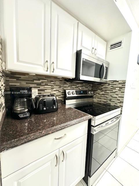 3505 S Ocean Dr Unit 419, Hollywood, FL 33019 - kitchen with stainless steel appliances, white cabinets, tasteful backsplash, light tile patterned flooring, and dark stone counters