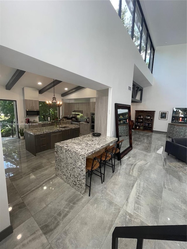 5811 SW 33rd Ter, Hollywood, FL 33312 - kitchen featuring appliances with stainless steel finishes, a high ceiling, a chandelier, an island with sink, and stone counters