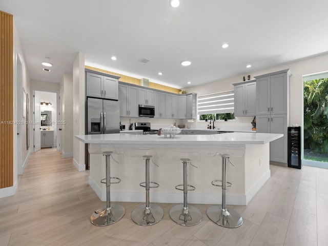 18100 SW 175th St, Miami, FL 33187 - kitchen featuring appliances with stainless steel finishes, a kitchen bar, wine cooler, light wood-type flooring, and gray cabinetry