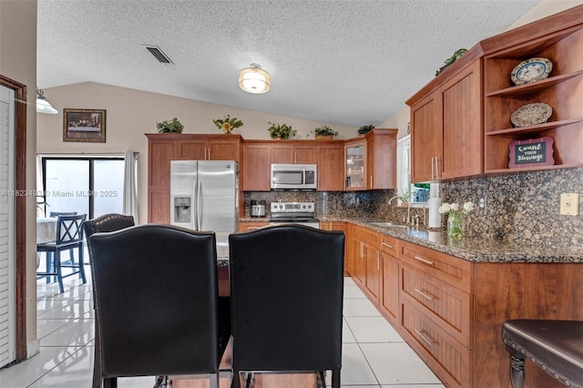 14548 SW 98th Ter, Miami, FL 33186 - kitchen with stainless steel appliances, vaulted ceiling, brown cabinetry, backsplash, and light tile patterned floors