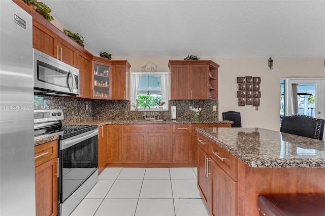 14548 SW 98th Ter, Miami, FL 33186 - kitchen featuring stainless steel appliances, brown cabinetry, healthy amount of natural light, open shelves, and a textured ceiling