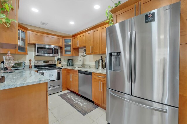 13705 SW 84th St Unit H, Miami, FL 33183 - kitchen with appliances with stainless steel finishes, light stone counters, light tile patterned floors, glass insert cabinets, and brown cabinets