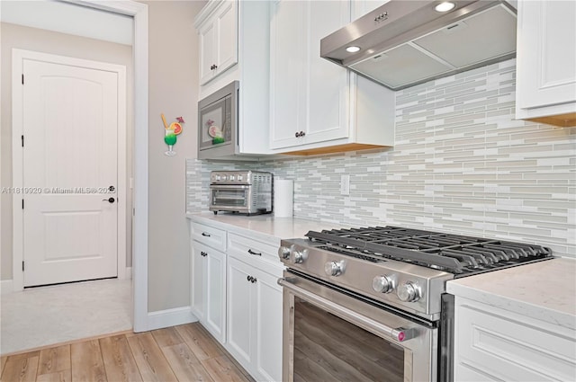 42250 Ramble Rd, Punta Gorda, FL 33982 - kitchen with gas range, extractor fan, light wood finished floors, white cabinetry, and backsplash