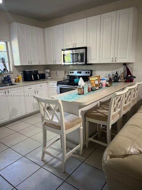 4812 Washington St Unit 8, Hollywood, FL 33021 - kitchen with stainless steel appliances, white cabinets, a kitchen bar, and light tile patterned floors