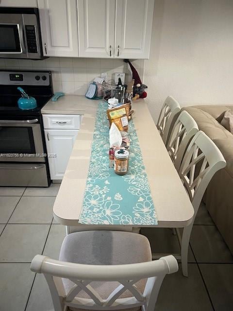 4812 Washington St Unit 8, Hollywood, FL 33021 - kitchen featuring appliances with stainless steel finishes, light tile patterned flooring, light countertops, white cabinetry, and tasteful backsplash