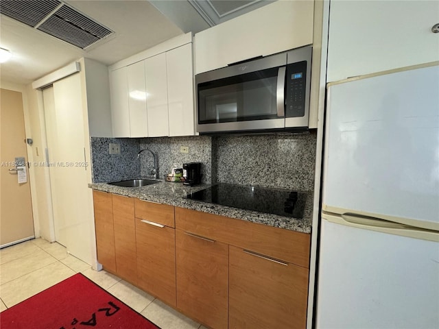 19201 Collins Ave Unit 1137, Sunny Isles Beach, FL 33160 - kitchen with freestanding refrigerator, stainless steel microwave, black electric stovetop, decorative backsplash, and brown cabinets