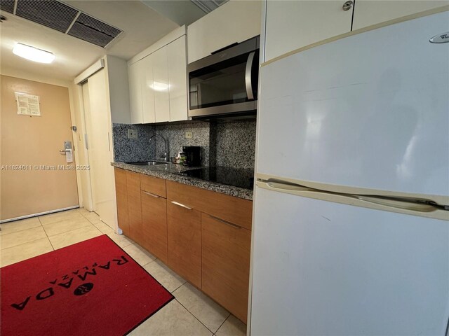 19201 Collins Ave Unit 1137, Sunny Isles Beach, FL 33160 - kitchen with freestanding refrigerator, stainless steel microwave, black electric cooktop, tasteful backsplash, and light tile patterned floors