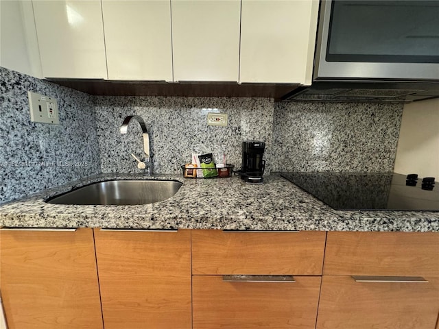 19201 Collins Ave Unit 1137, Sunny Isles Beach, FL 33160 - kitchen with stainless steel microwave, black electric cooktop, light stone counters, backsplash, and white cabinets
