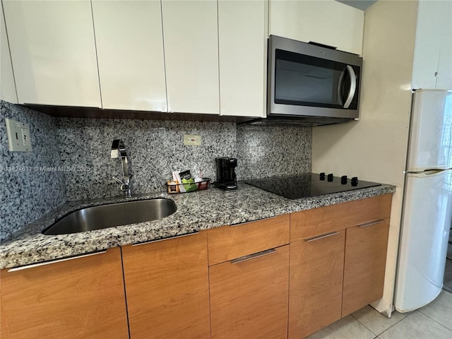 19201 Collins Ave Unit 1137, Sunny Isles Beach, FL 33160 - kitchen featuring stainless steel microwave, freestanding refrigerator, light stone countertops, black electric cooktop, and tasteful backsplash