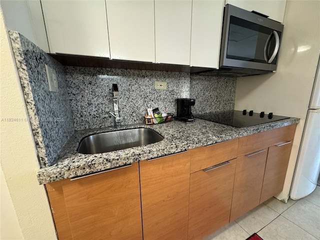 19201 Collins Ave Unit 1137, Sunny Isles Beach, FL 33160 - kitchen featuring stainless steel microwave, black electric cooktop, backsplash, dark stone countertops, and white cabinets