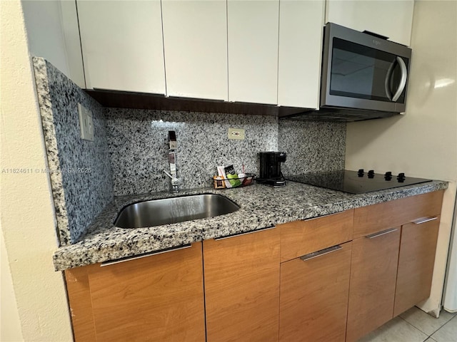 19201 Collins Ave Unit 1137, Sunny Isles Beach, FL 33160 - kitchen featuring stainless steel microwave, black electric cooktop, backsplash, dark stone countertops, and white cabinets
