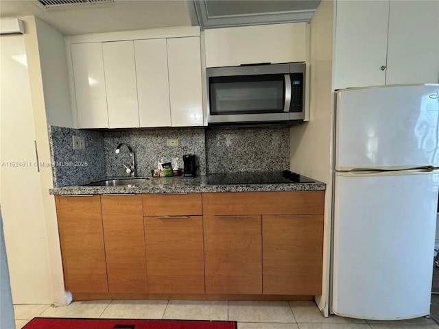19201 Collins Ave Unit 1137, Sunny Isles Beach, FL 33160 - kitchen featuring freestanding refrigerator, stainless steel microwave, tasteful backsplash, light tile patterned floors, and dark stone countertops