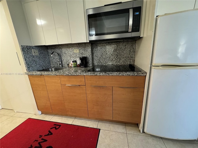 19201 Collins Ave Unit 1137, Sunny Isles Beach, FL 33160 - kitchen featuring freestanding refrigerator, stainless steel microwave, black electric stovetop, decorative backsplash, and light tile patterned floors