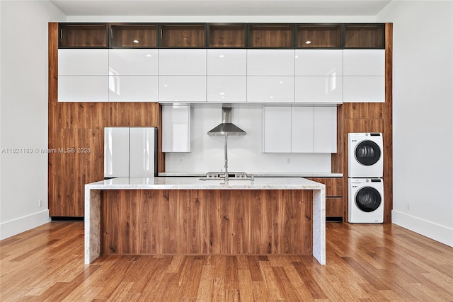9741 SE Gomez Ave, Hobe Sound, FL 33455 - kitchen with stacked washer / drying machine, modern cabinets, freestanding refrigerator, wall chimney exhaust hood, and light wood-style floors
