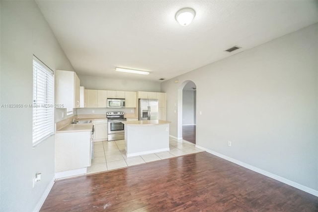 10870 SW 229th St, Miami, FL 33170 - kitchen featuring appliances with stainless steel finishes, arched walkways, a kitchen island, light countertops, and light wood-style floors