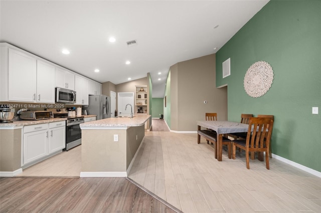 4728 Adrienne St, Sebring, FL 33872 - kitchen with appliances with stainless steel finishes, lofted ceiling, white cabinetry, an island with sink, and light wood finished floors