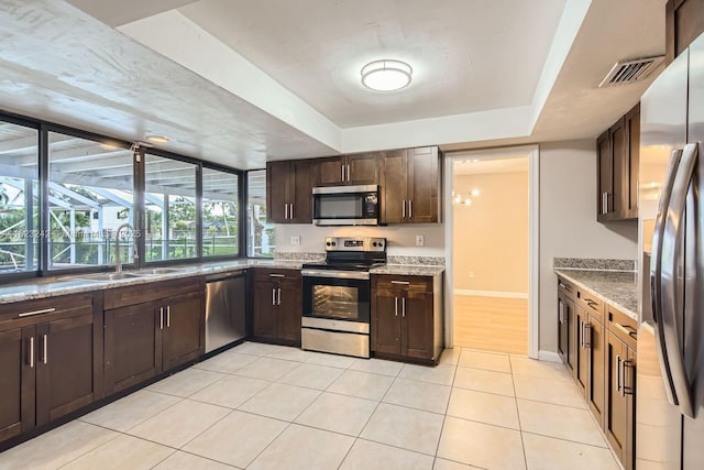 1708 NW 84th Dr, Coral Springs, FL 33071 - kitchen featuring appliances with stainless steel finishes, a tray ceiling, dark brown cabinets, light tile patterned floors, and light stone countertops