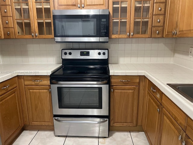 3841 NW 7th Ct, Lauderhill, FL 33311 - kitchen with stainless steel appliances, brown cabinetry, and light tile patterned floors