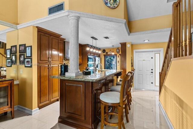 10091 SW 137th Pl, Miami, FL 33186 - kitchen featuring ornate columns, a breakfast bar, stone counters, a kitchen island with sink, and decorative light fixtures