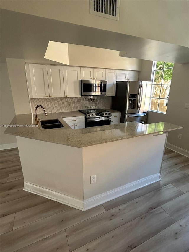 2921 NE 185th St Unit 1205, Aventura, FL 33180 - kitchen with stainless steel appliances, light stone counters, a peninsula, white cabinets, and decorative backsplash