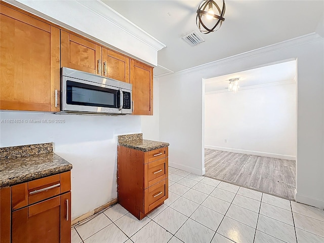 6464 Mcclellan St, Hollywood, FL 33024 - kitchen with stainless steel microwave, crown molding, brown cabinetry, light tile patterned floors, and dark stone countertops