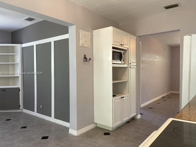 5433 NE 5th Ave, Oakland Park, FL 33334 - kitchen featuring tile patterned floors, stainless steel microwave, and white cabinetry