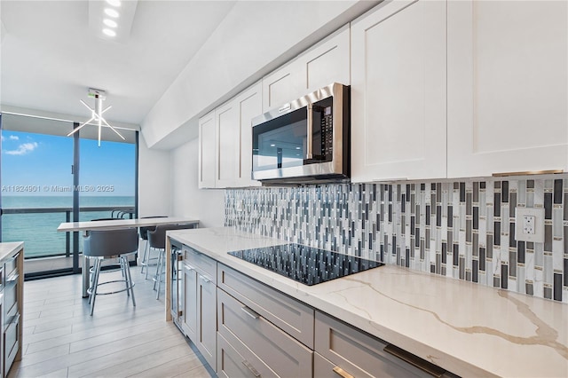 9455 Collins Ave Unit 809, Surfside, FL 33154 - kitchen with stainless steel microwave, black electric stovetop, tasteful backsplash, floor to ceiling windows, and light stone counters