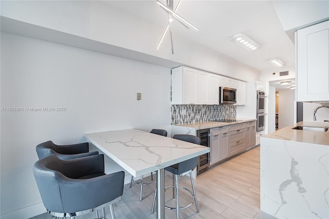 9455 Collins Ave Unit 809, Surfside, FL 33154 - kitchen with appliances with stainless steel finishes, a breakfast bar area, decorative backsplash, light stone counters, and beverage cooler