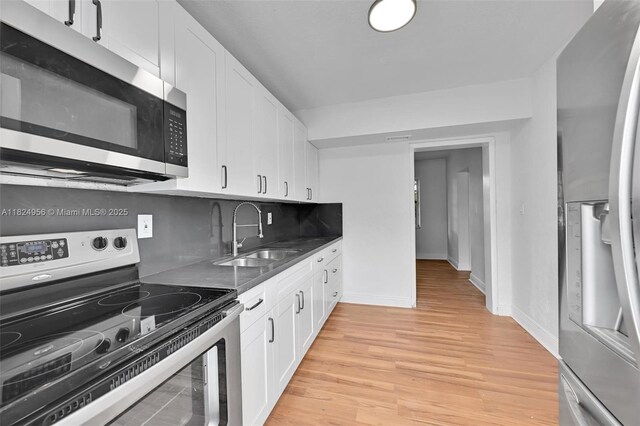 1355 NW 121st St, North Miami, FL 33167 - kitchen with appliances with stainless steel finishes, white cabinets, light wood-type flooring, dark countertops, and tasteful backsplash