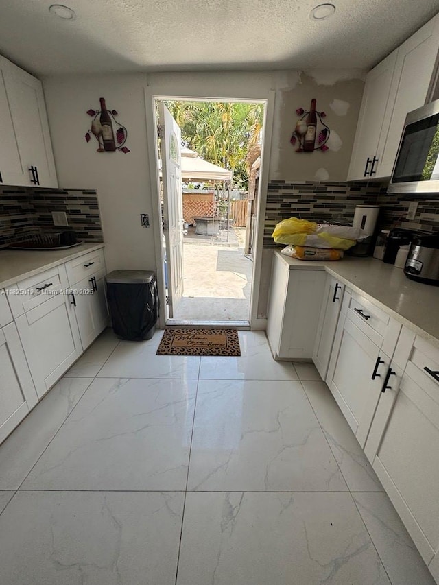791 E 18th St, Hialeah, FL 33013 - kitchen with stainless steel microwave, light marble finish floors, tasteful backsplash, a textured ceiling, and white cabinets