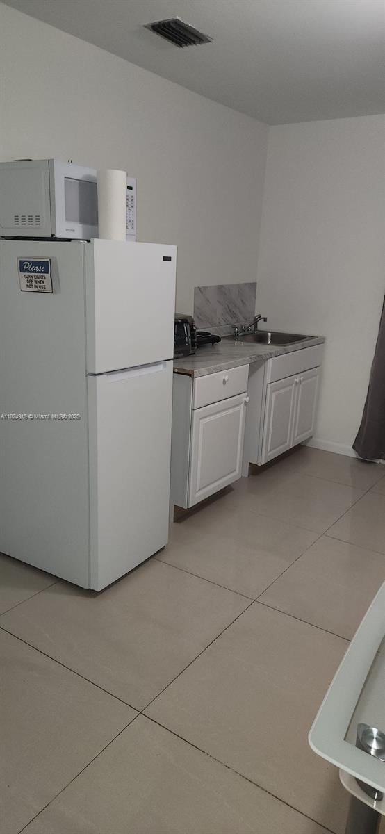 1607 Moffett St, Hollywood, FL 33020 - kitchen featuring freestanding refrigerator, light tile patterned flooring, and white cabinetry