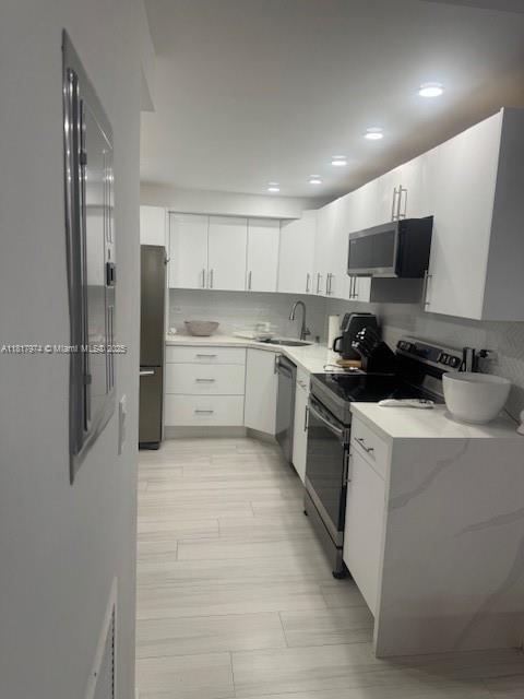 6039 Collins Ave Unit 1516, Miami Beach, FL 33140 - kitchen with range with electric stovetop, stainless steel dishwasher, white cabinets, backsplash, and freestanding refrigerator