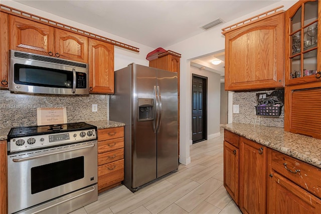11700 Sheridan St, Pembroke Pines, FL 33026 - kitchen with appliances with stainless steel finishes, brown cabinets, light stone counters, glass insert cabinets, and tasteful backsplash
