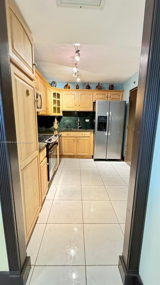 6039 Collins Ave Unit 923, Miami Beach, FL 33140 - kitchen featuring appliances with stainless steel finishes, light brown cabinetry, dark countertops, light tile patterned floors, and glass insert cabinets