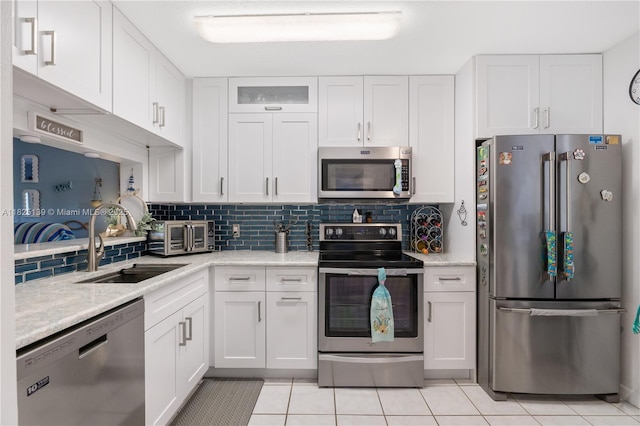 5725 Pelican Pointe, Sebastian, FL 32958 - kitchen featuring appliances with stainless steel finishes, white cabinetry, light tile patterned flooring, decorative backsplash, and light stone counters