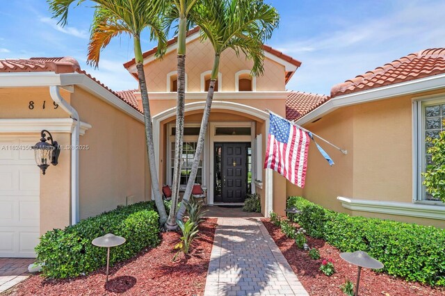 819 SW Bromelia Ter, Stuart, FL 34997 - view of exterior entry with stucco siding, a tiled roof, and an attached garage