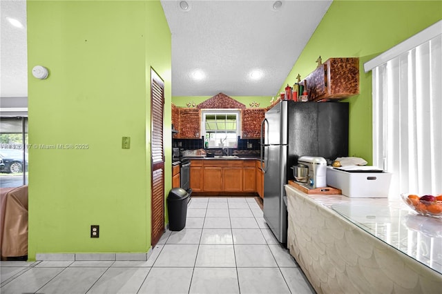 5610 NW 54th Ave, Tamarac, FL 33319 - kitchen featuring a textured ceiling, appliances with stainless steel finishes, light tile patterned flooring, brown cabinets, and tasteful backsplash
