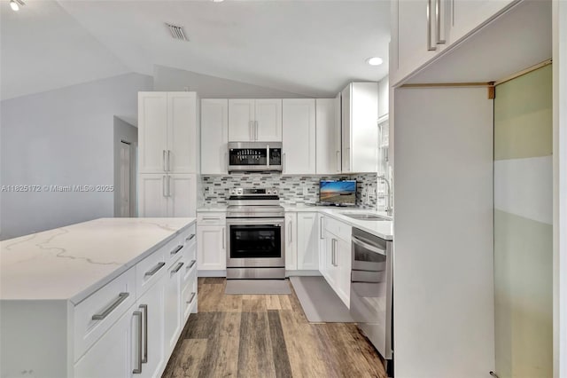 509 SW Hamburg Ter, Port St Lucie, FL 34984 - kitchen with appliances with stainless steel finishes, light wood-style flooring, lofted ceiling, tasteful backsplash, and light stone counters