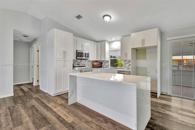 509 SW Hamburg Ter, Port St Lucie, FL 34984 - kitchen with appliances with stainless steel finishes, dark wood-style flooring, lofted ceiling, white cabinets, and backsplash