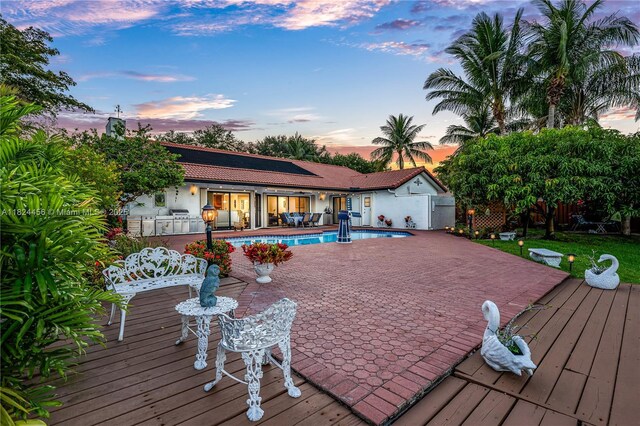 1460 NW 99th Ave, Plantation, FL 33322 - back of property at dusk featuring a wooden deck, an outdoor pool, stucco siding, and a tiled roof