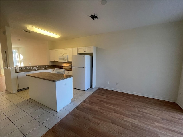 3550 Oleander Ter, Riviera Beach, FL 33404 - kitchen with white appliances, dark countertops, a kitchen island, white cabinets, and light tile patterned floors