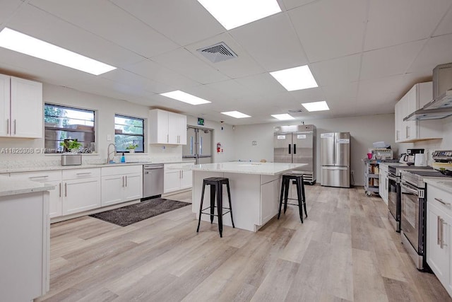 3420 NW 21st Ct, Coconut Creek, FL 33066 - kitchen with stainless steel appliances, a kitchen breakfast bar, light wood-type flooring, white cabinetry, and a center island