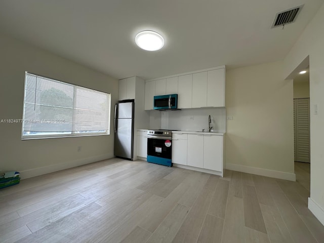 1514 SW 6th St, Miami, FL 33135 - kitchen featuring stainless steel appliances, white cabinets, light wood finished floors, and modern cabinets