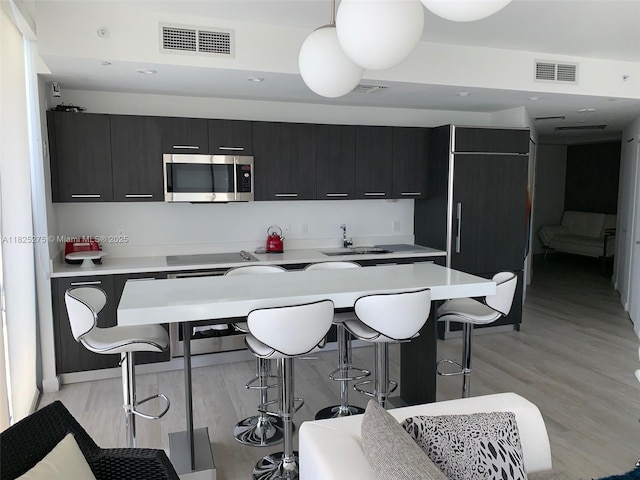 55 SW 9th St Unit 2706, Miami, FL 33130 - kitchen with stainless steel microwave, dark cabinetry, a kitchen breakfast bar, light wood-style flooring, and light countertops