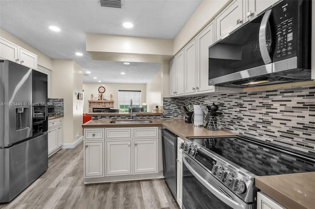 11664 NW 19th Dr, Coral Springs, FL 33071 - kitchen featuring appliances with stainless steel finishes, backsplash, a peninsula, light wood-style floors, and white cabinetry