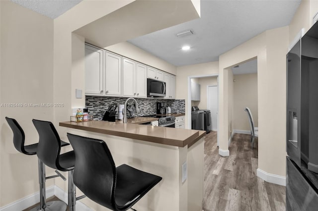 11664 NW 19th Dr, Coral Springs, FL 33071 - kitchen with stainless steel appliances, separate washer and dryer, tasteful backsplash, light wood finished floors, and a peninsula