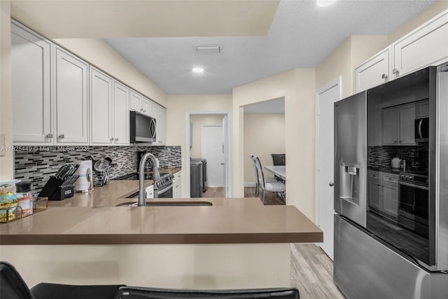 11664 NW 19th Dr, Coral Springs, FL 33071 - kitchen with appliances with stainless steel finishes, tasteful backsplash, a peninsula, white cabinets, and light wood-type flooring